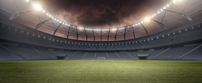 Empty floodlit football stadium with a broad grass pitch