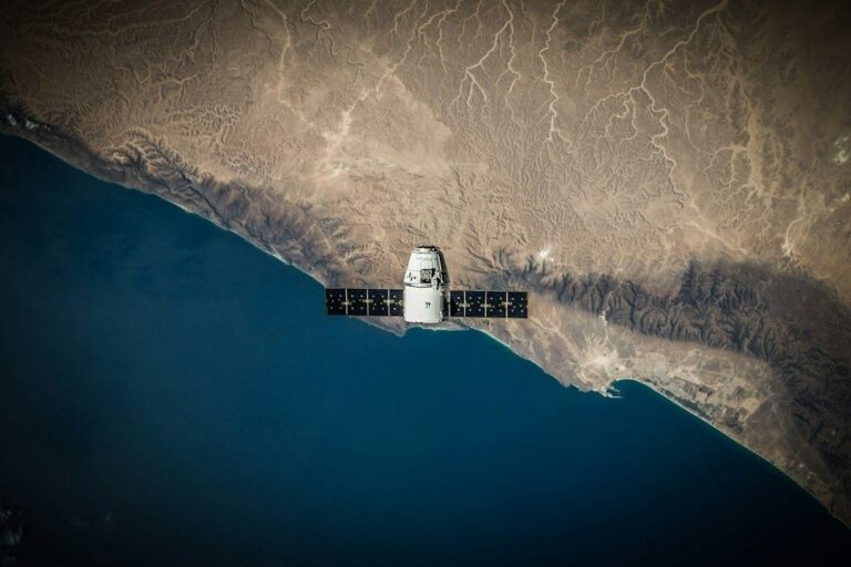 Satellite with solar panels over a desert coastline and dark blue sea